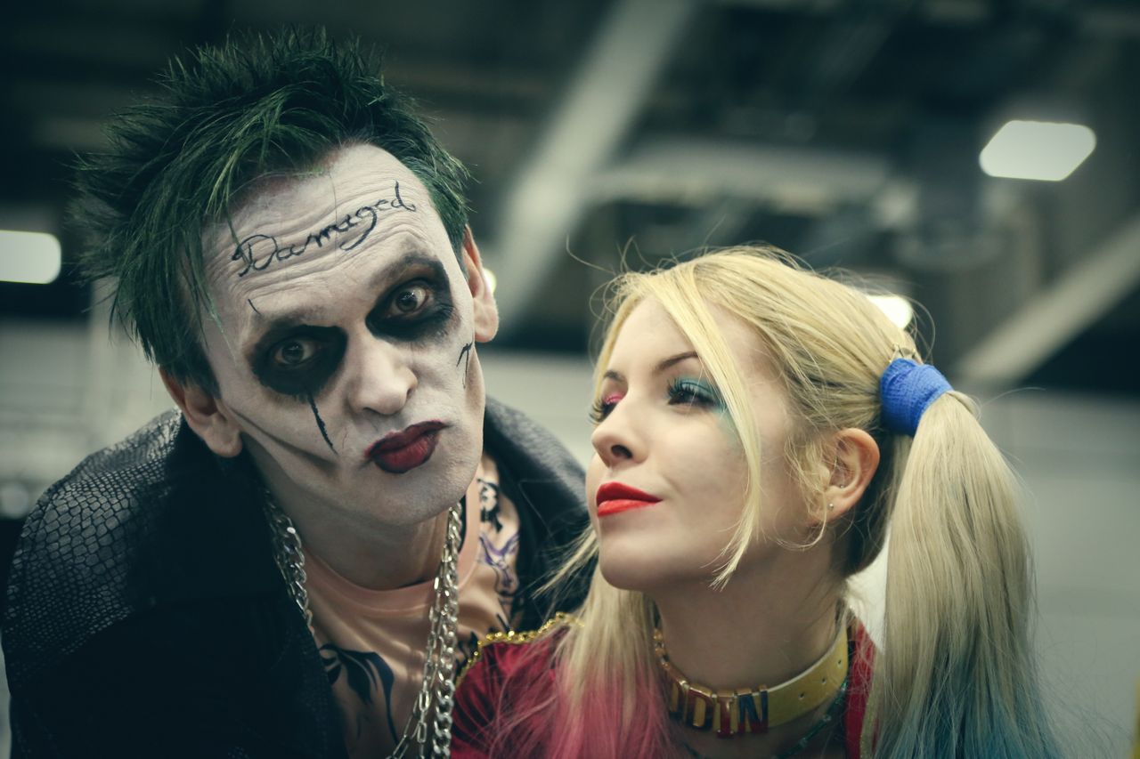 A couple in detailed Halloween cosplay with striking makeup and costumes pose together indoors.