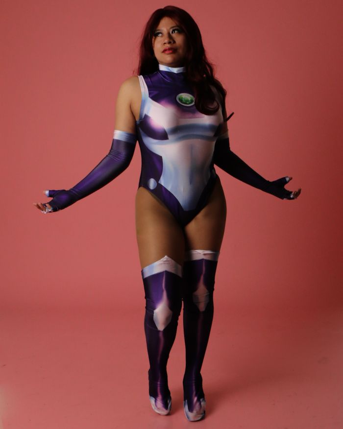 Cosplayer posing in a futuristic costume against a pink studio backdrop.