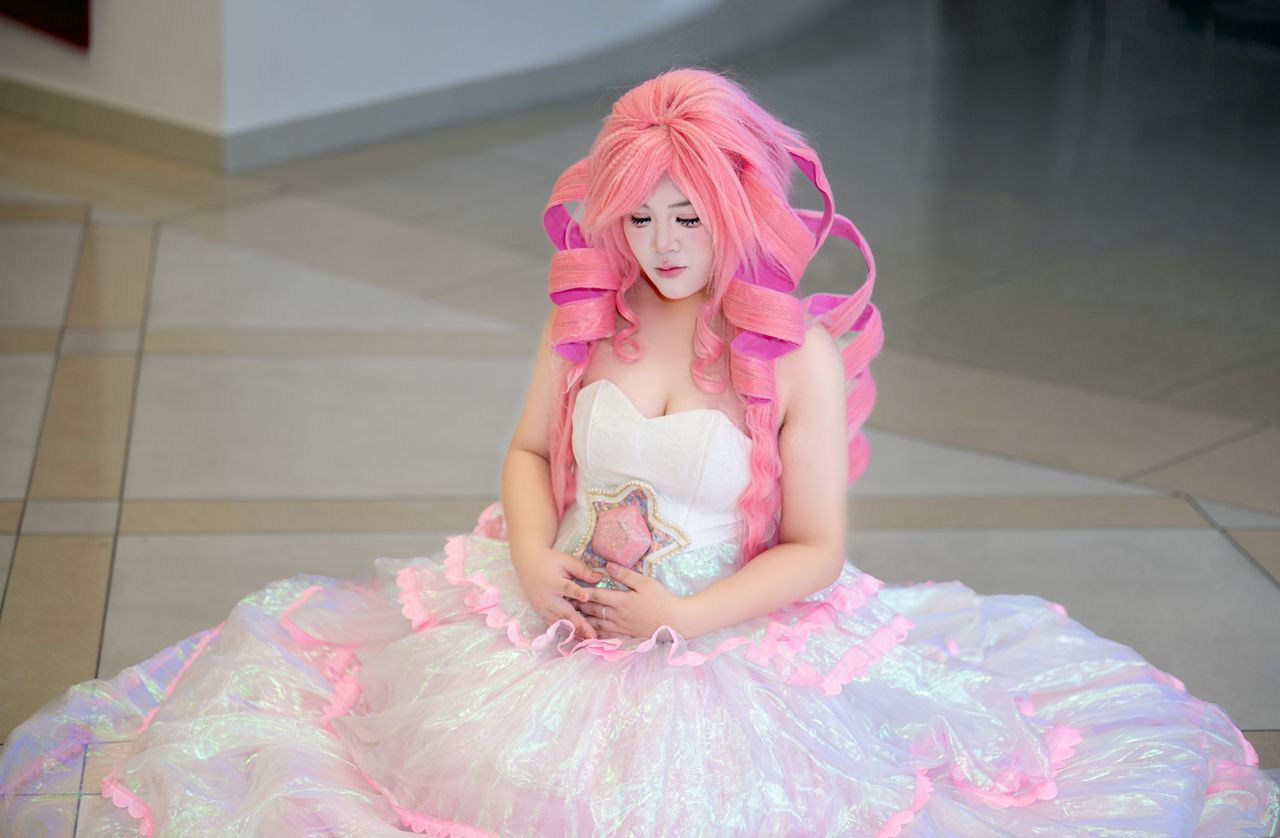 A person in vibrant cosplay with pink hair and a stunning dress indoors.